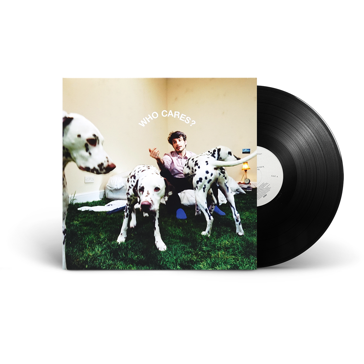 A vinyl record partially pulled from its album sleeve, showing the cover art of 'Who Cares?' with a man sitting between three Dalmatian dogs. The black vinyl disc is visible on the right