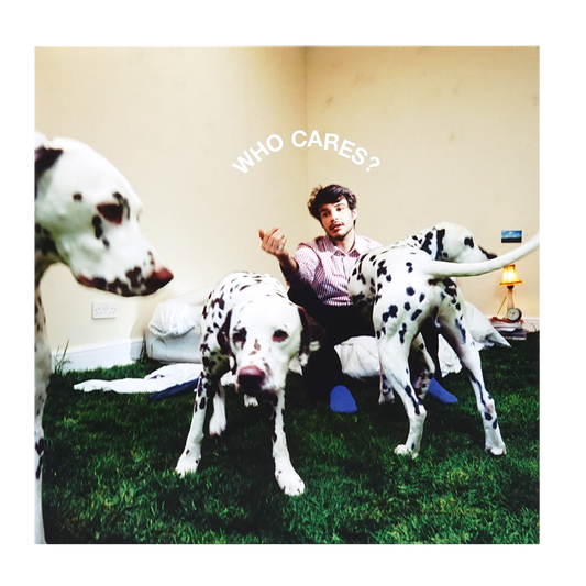 Rex Orange County sitting on the floor in a room with three Dalmatian dogs, with the text 'WHO CARES?' written above him.